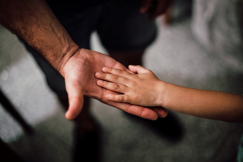 Close-up of a child's hand resting gently on a man's hand, symbolizing love and support.